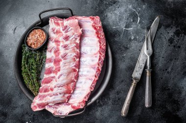Raw rack of pork spare ribs in steel kitchen tray. Black background. Top view.