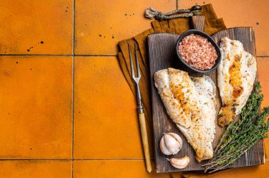 Roast sea red perch fillet, redfish fish on wooden board. Orange background. Top view. Copy space.