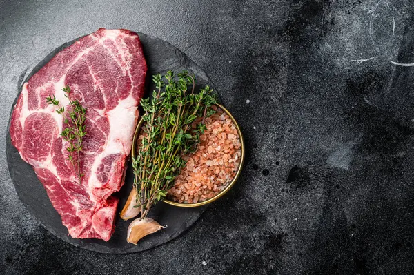 Pork loin steak, raw neck meat with thyme and salt. Black background. Top view. Copy space.