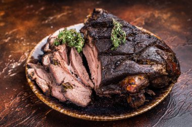 Pişmiş ve dilimlenmiş geyik bacağı. Tabağında kemik olan geyik eti kızartması. kahverengi arka plan. en üstteki görünüm.