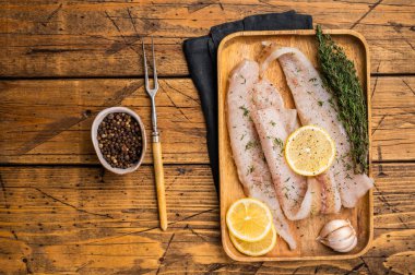 Çiğ Pollock ve Hake balık filetoları ahşap bir tahtanın üzerinde pişirilmeye hazır otlarla birlikte. Ahşap arka plan. en üstteki görünüm.