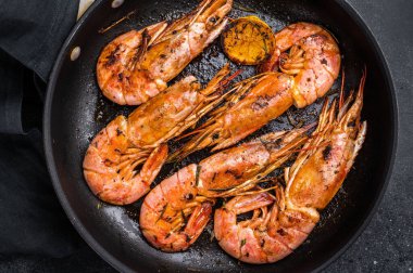 Tavada kızartılmış kırmızı Arjantin karidesi, Karidesler Langostino Austral ve otlar. Siyah arka plan. en üstteki görünüm.