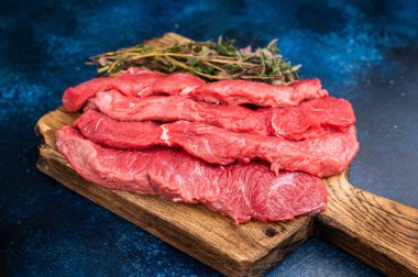 Kırsal bir tabakta güzelce dilimlenmiş çiğ bufalo eti, rengini ve kalitesini gözler önüne seriyor, ızgara veya kızartma için mükemmel. mavi arka plan. en üstteki görünüm.