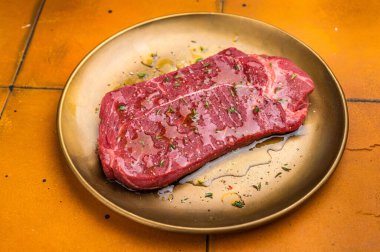 Zeytinyağı ve otlarla marine edilmiş çiğ sığır filetosu ya da biftek. turuncu arka plan. en üstteki görünüm.