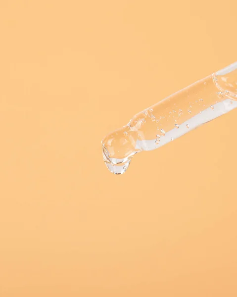 pipette with a drop of oil on a yellow background closeup