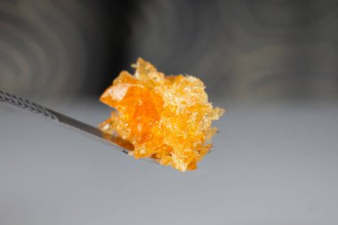 amber yellow cannabis wax concentrate dripping from the dabbing tool closeup.
