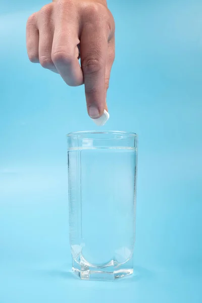 glass cup with water and a hand with a pill on blue background medication.
