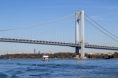 Staten Island, NY, United States - October 6, 2022: A pleasure craft passing under the Verrazzano-Narrows Bridge exiting New York Harbor as two container ships enter. Bridge exiting New York Harbor.