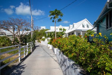 Hope Town, Abacos, Bahamas - March 26, 2024:  Plants and houses line a narrow street in Hope Town, Bahamas clipart