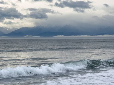 Dalgalar kopuyor ve uzak dağlar Pasifik 'in kuzeybatısında bulutlu gökyüzü var.