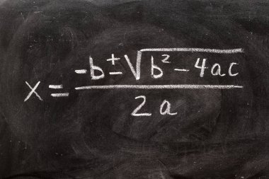 Karatahtaya tebeşir ve matematiksel formüllerle el yazısıyla yazılmış ikinci dereceden denklemler