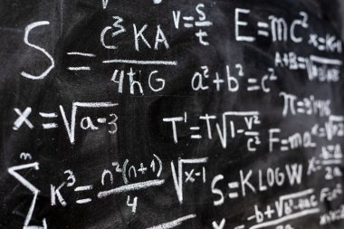 Matematiksel denklemler ve fizik formülleri tahtaya tebeşirle yazılmış.