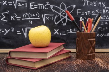 Okula fizik ve matematik formülleriyle yazılmış karatahta geçmişi olan kitaplar, kalemler ve elmalarla dönmek.
