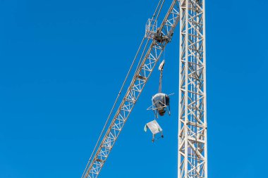 Büyük vinç, arka planda mavi gökyüzü olan bir inşaat sahasında inşaat malzemeleri taşıyor.