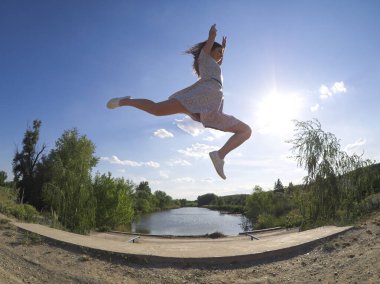 Formda bir kız açık havada, güneşli gökyüzünün altında çiçeklerle dans ediyor.