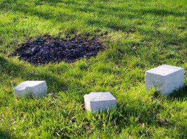 Terk edilmiş kamp şöminesi çimento blokları ve külleri olan yeşil bir çimenlikte.