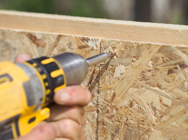 Carpenter working with yellow electric screwdriver on a wood board