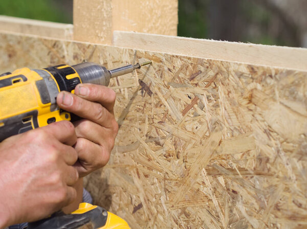 Carpenter working with yellow electric screwdriver on a wood board