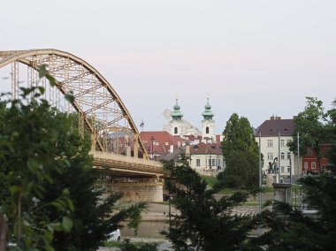 Macaristan 'ın Gyor kentindeki Raba Nehri boyunca uzanan tarihi Kossuth Köprüsü, Loyola' nın Benediktine Kilisesi 'nin ikiz kuleleri ve arka plandaki binalar - 5 Mayıs 2018