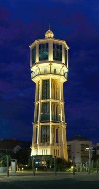 İkonik Siofok Su Kulesi, Macaristan 'ın Sifok kentinin göbeğindeki eşsiz sekizgen mimarisini gözler önüne sererek, derin mavi bir alacakaranlık gökyüzüne parlak bir şekilde aydınlatmıştır..