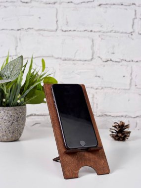 Akıllı telefon beyaz bir masadaki ahşap bir standın üzerinde duruyor. Tahta akıllı telefon standı. Boşluğu kopyala.