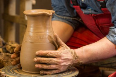Çömlekçinin elleri çömlekçi çarkında kille çalışıyor, kâse oluşturuyor. Geleneksel çömlek, el sanatları, otantik atmosfer