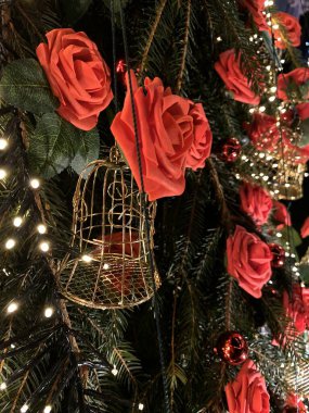 Fotoğrafta, kırmızı güller ve sayısız küçük beyaz ışıkla aydınlatılmış küçük altın kuş kafesleriyle süslenmiş bir Noel ağacı yer alıyor. Arka planda, beyaz ışıklara sarılmış başka bir ağaç festival atmosferine katkı sağlıyor. Kombinasyon: 
