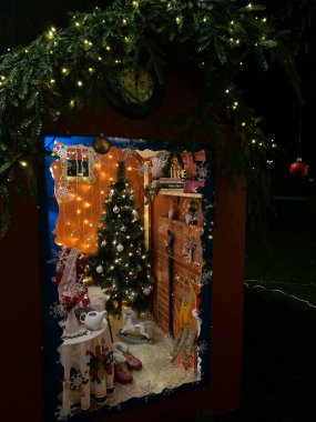 Fotoğrafta, tatil sezonu için dekore edilmiş Noel temalı bir çocuk oyun evi yer alıyor. Tahta oyun evinin pencereleri ve Noel çelenkleri ve çelenklerle süslenmiş bir kapısı var. Tiyatronun çatısı parlayan ışıklarla dolu.