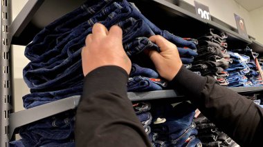 Moda bir giyim mağazasında kot pantolon almak için kapüşonlu bir adam. Moda alışverişi, modern yaşam tarzı, gündelik moda, ergen modası, perakende deneyimi. Bir Giyim Mağazasında Birçok Elbise Askısı Tutan Kız, Alışveriş Konsepti, Moda