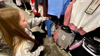 Moda bir giyim mağazasında kot pantolon almak için kapüşon giyen genç bir kadın. Moda alışverişi, modern yaşam tarzı, gündelik moda, ergen modası, perakende deneyimi. Bir Giyim Mağazasında Çok Giysi Askısı Tutan Kız, Alışveriş Konsepti, Fa