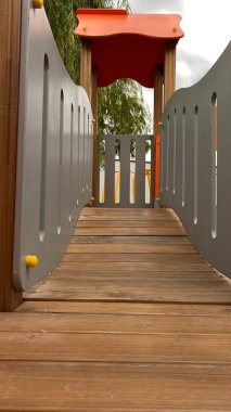 Renkli bir kaydırak, tırmanma merdiveni, küçük ahşap oyun evi ve köprü yapısı olan modern açık hava çocukları için oyun alanı. Kamu parkında ya da eğlence alanında geçen bu ekipman fiziksel aktiviteyi, hayal gücünü ve sosyal etkileşimi teşvik eder..