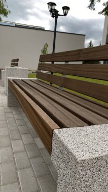 Modern bir konut binasının peyzajlı avlusunda yer alan beton desteklerden ve ahşap oturma yüzeyinden oluşan çağdaş bir tezgah. Bu bank konfor, rahatlama ve kentsel aes için tasarlanmış iyi korunmuş bir kamu alanının parçasıdır.