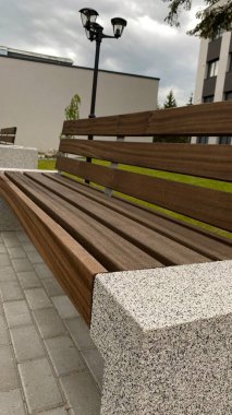 Modern bir konut binasının peyzajlı avlusunda yer alan beton desteklerden ve ahşap oturma yüzeyinden oluşan çağdaş bir tezgah. Bu bank konfor, rahatlama ve kentsel aes için tasarlanmış iyi korunmuş bir kamu alanının parçasıdır.