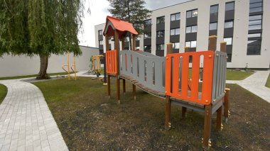 Renkli bir kaydırak, tırmanma merdiveni, küçük ahşap oyun evi ve köprü yapısı olan modern açık hava çocukları için oyun alanı. Kamu parkında ya da eğlence alanında geçen bu ekipman fiziksel aktiviteyi, hayal gücünü ve sosyal etkileşimi teşvik eder..