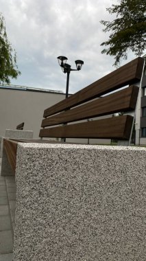 Modern bir konut binasının peyzajlı avlusunda yer alan beton desteklerden ve ahşap oturma yüzeyinden oluşan çağdaş bir tezgah. Bu bank konfor, rahatlama ve kentsel aes için tasarlanmış iyi korunmuş bir kamu alanının parçasıdır.