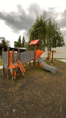 Renkli bir kaydırak, tırmanma merdiveni, küçük ahşap oyun evi ve köprü yapısı olan modern açık hava çocukları için oyun alanı. Kamu parkında ya da eğlence alanında geçen bu ekipman fiziksel aktiviteyi, hayal gücünü ve sosyal etkileşimi teşvik eder..