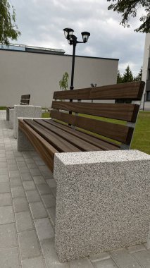 Modern bir konut binasının peyzajlı avlusunda yer alan beton desteklerden ve ahşap oturma yüzeyinden oluşan çağdaş bir tezgah. Bu bank konfor, rahatlama ve kentsel aes için tasarlanmış iyi korunmuş bir kamu alanının parçasıdır.