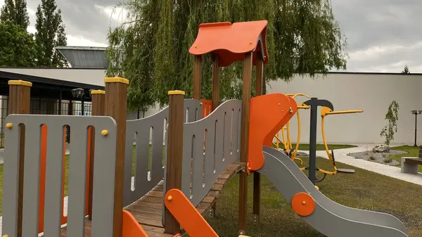 Renkli bir kaydırak, tırmanma merdiveni, küçük ahşap oyun evi ve köprü yapısı olan modern açık hava çocukları için oyun alanı. Kamu parkında ya da eğlence alanında geçen bu ekipman fiziksel aktiviteyi, hayal gücünü ve sosyal etkileşimi teşvik eder..