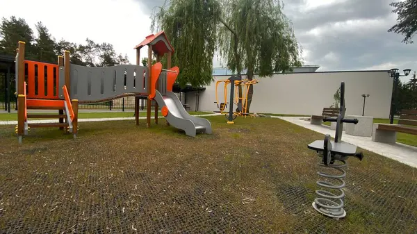 Renkli bir kaydırak, tırmanma merdiveni, küçük ahşap oyun evi ve köprü yapısı olan modern açık hava çocukları için oyun alanı. Kamu parkında ya da eğlence alanında geçen bu ekipman fiziksel aktiviteyi, hayal gücünü ve sosyal etkileşimi teşvik eder..