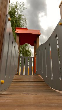 Renkli bir kaydırak, tırmanma merdiveni, küçük ahşap oyun evi ve köprü yapısı olan modern açık hava çocukları için oyun alanı. Kamu parkında ya da eğlence alanında geçen bu ekipman fiziksel aktiviteyi, hayal gücünü ve sosyal etkileşimi teşvik eder..