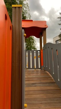 Renkli bir kaydırak, tırmanma merdiveni, küçük ahşap oyun evi ve köprü yapısı olan modern açık hava çocukları için oyun alanı. Kamu parkında ya da eğlence alanında geçen bu ekipman fiziksel aktiviteyi, hayal gücünü ve sosyal etkileşimi teşvik eder..