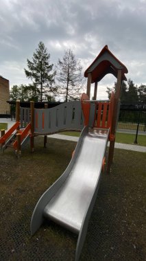 Renkli bir kaydırak, tırmanma merdiveni, küçük ahşap oyun evi ve köprü yapısı olan modern açık hava çocukları için oyun alanı. Kamu parkında ya da eğlence alanında geçen bu ekipman fiziksel aktiviteyi, hayal gücünü ve sosyal etkileşimi teşvik eder..