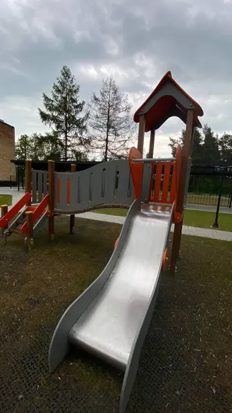 Renkli bir kaydırak, tırmanma merdiveni, küçük ahşap oyun evi ve köprü yapısı olan modern açık hava çocukları için oyun alanı. Kamu parkında ya da eğlence alanında geçen bu ekipman fiziksel aktiviteyi, hayal gücünü ve sosyal etkileşimi teşvik eder..