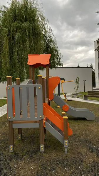 Renkli bir kaydırak, tırmanma merdiveni, küçük ahşap oyun evi ve köprü yapısı olan modern açık hava çocukları için oyun alanı. Kamu parkında ya da eğlence alanında geçen bu ekipman fiziksel aktiviteyi, hayal gücünü ve sosyal etkileşimi teşvik eder..