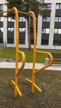 Modern bir konut avlusuna yerleştirilmiş sağlam metal paralel barlar, bir çocuk oyun parkının yakınında yer alıyor. Vücut ağırlık egzersizleri ve sokak fitness rutinleri için tasarlanan ekipman, fiziksel gelişimi destekliyor ve aktif bir kentsel yaşamı teşvik ediyor.
