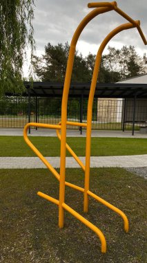 Modern bir konut avlusuna yerleştirilmiş sağlam metal paralel barlar, bir çocuk oyun parkının yakınında yer alıyor. Vücut ağırlık egzersizleri ve sokak fitness rutinleri için tasarlanan ekipman, fiziksel gelişimi destekliyor ve aktif bir kentsel yaşamı teşvik ediyor.