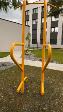 Modern bir konut avlusuna yerleştirilmiş sağlam metal paralel barlar, bir çocuk oyun parkının yakınında yer alıyor. Vücut ağırlık egzersizleri ve sokak fitness rutinleri için tasarlanan ekipman, fiziksel gelişimi destekliyor ve aktif bir kentsel yaşamı teşvik ediyor.