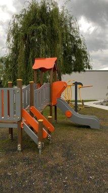 Renkli bir kaydırak, tırmanma merdiveni, küçük ahşap oyun evi ve köprü yapısı olan modern açık hava çocukları için oyun alanı. Kamu parkında ya da eğlence alanında geçen bu ekipman fiziksel aktiviteyi, hayal gücünü ve sosyal etkileşimi teşvik eder..