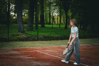 Genç bir kız açık hava kil kortunda tenis topuna raketle vuruyor. Saray yeşil bir orman ve tel örgü ile çevrili. Sıradan bir kot pantolon ve beyaz bir tişört giyip bahar etkinliğinin tadını çıkarıyor.. 