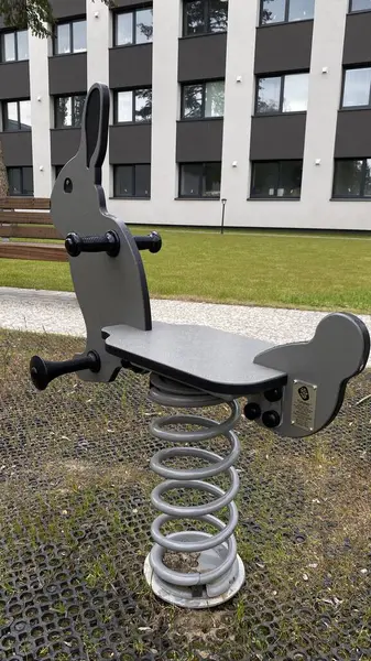 Modern bir çocuk parkına yerleştirilmiş tavşan şeklinde renkli bir yay binicisi. Güvenli açık hava oyunları ve fiziksel aktiviteler için tasarlanan bu araç gereç, küçük çocuklarda denge ve koordinasyon geliştirmeye yardımcı oluyor. Kamu parkında kullanmak için ideal